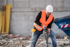 Concrete Demolition worker breaking up concrete with a tool and a hard hat on